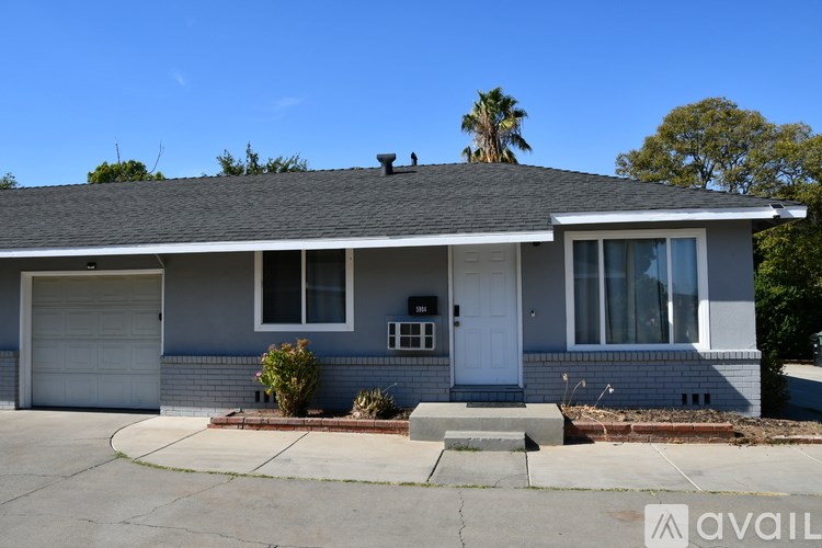 A house with a grey roof and a white door is available for rent.