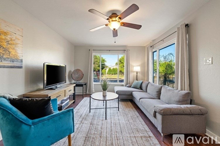 A living room with a blue chair, a grey couch, a television, and a ceiling fan.