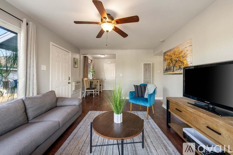 A living room with a grey couch, a blue chair, a wooden coffee table, and a ceiling fan.