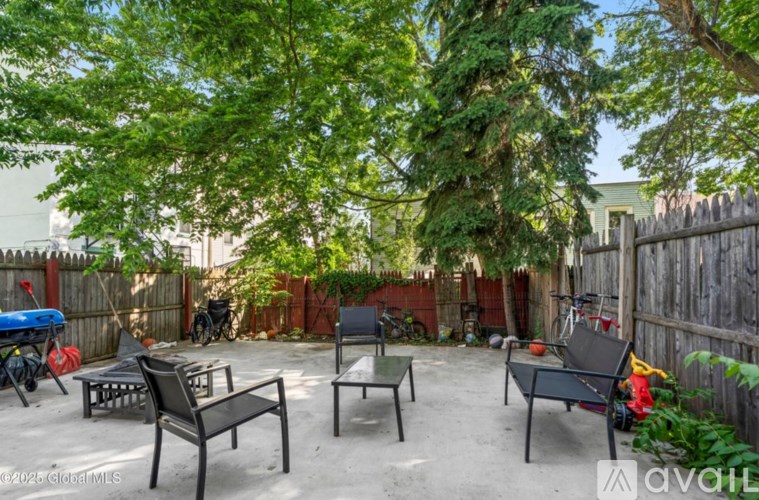 A backyard with a fence, a bicycle, a chair, a table and a bench.