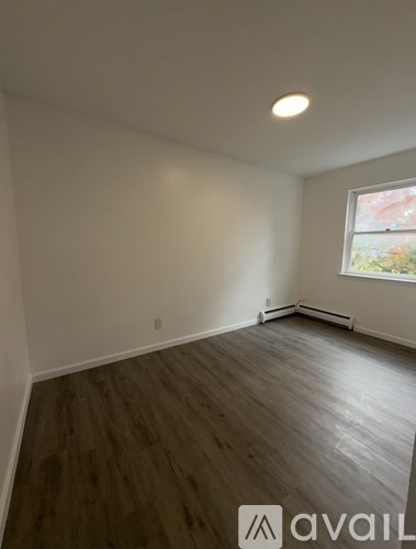 A room with wooden flooring and a window showing greenery outside.