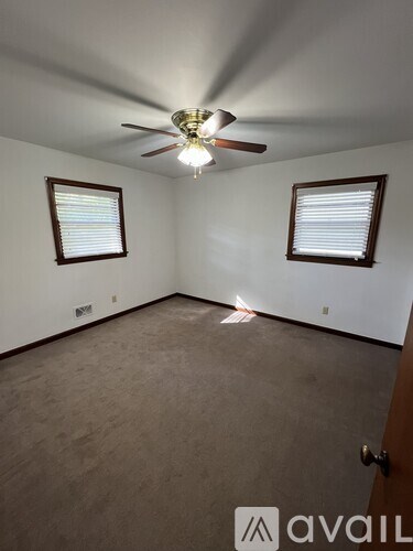 A room with a ceiling fan and two windows.