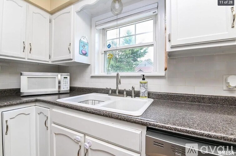 A kitchen with white cabinets and a window showing trees outside.