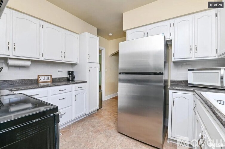 A kitchen with white cabinets and a stainless steel refrigerator.