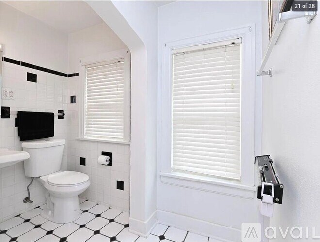 A white toilet with a black seat sits in a bathroom with white walls and a black and white checkered floor.