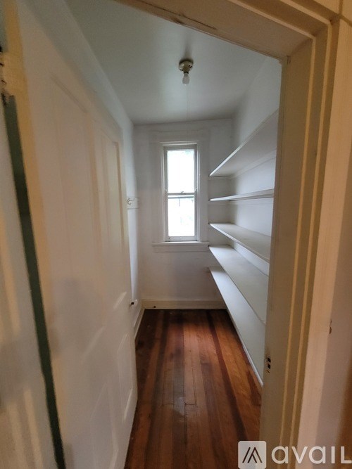 A narrow hallway with wooden floors and white walls.