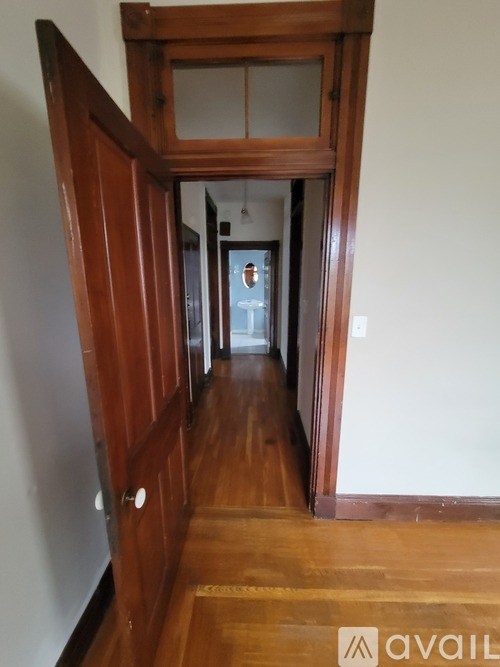 A hallway with a wooden floor and a door on the left.