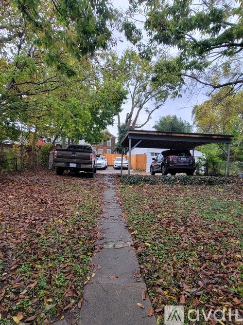 A sidewalk covered in fallen leaves with a car parked on the street.