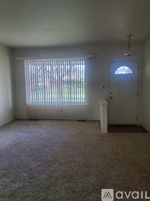 A room with a carpeted floor, a door, and a window with blinds.