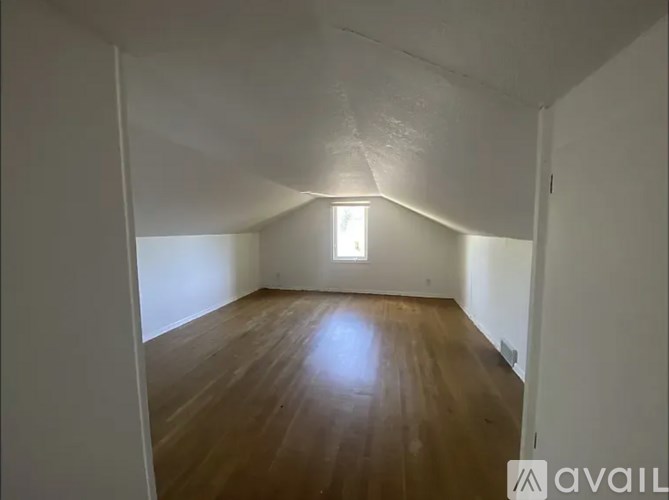 A room with wooden flooring and white walls, with a window in the middle.