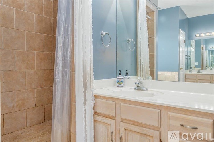 A bathroom with a beige tiled shower and a white sink vanity.