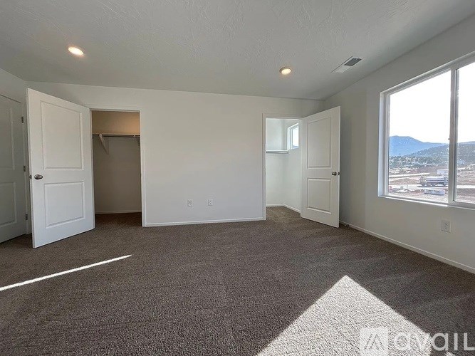 A room with white walls and carpeted floor with a mountain view through the window.