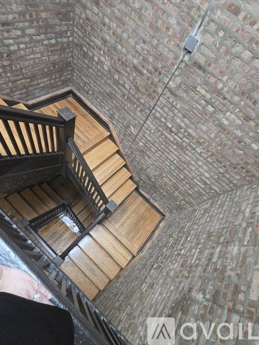 A wooden staircase with a metal railing leads up to a brick wall.