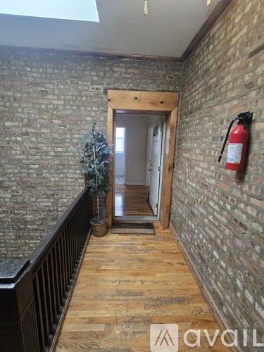 A hallway with a brick wall and wooden floor leading to a door.