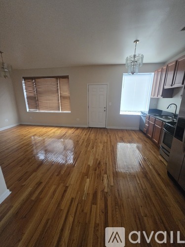 A room with wooden floors and a kitchen area in the background.