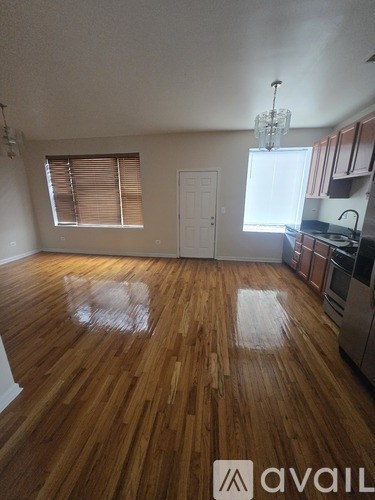 A room with wooden floors and a kitchen area in the background.