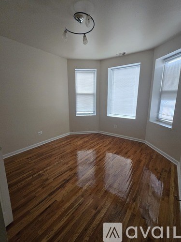 A room with wooden flooring and three windows.