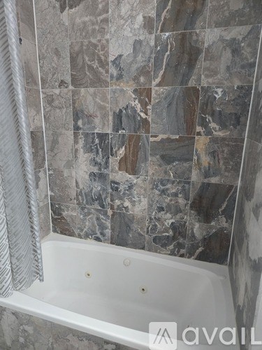 A bathroom with a marble tile wall and a white bathtub.
