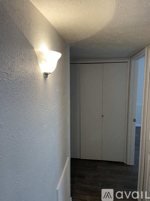 A white wall with a light on it and a white cupboard.