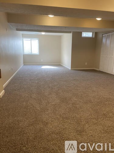 A carpeted room with a window and a door leading to another room.