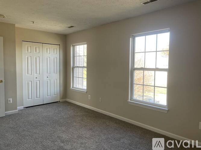 A room with a carpeted floor, a white door, and a window with a view of a tree.