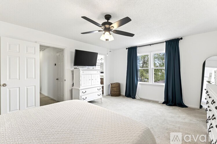 A bedroom with a large bed, a television, and a window with blue curtains.