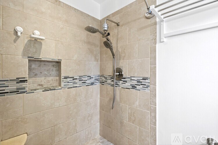 A beige tiled shower with a glass door and a white shower head.