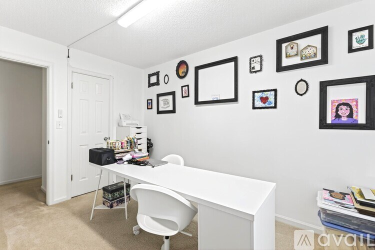 A white desk with a chair and a wall with pictures and a clock.