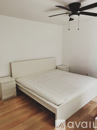 A bed with a white mattress and a white headboard is in a room with a ceiling fan.