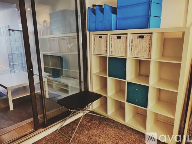 A room with a shelving unit and a black stool.