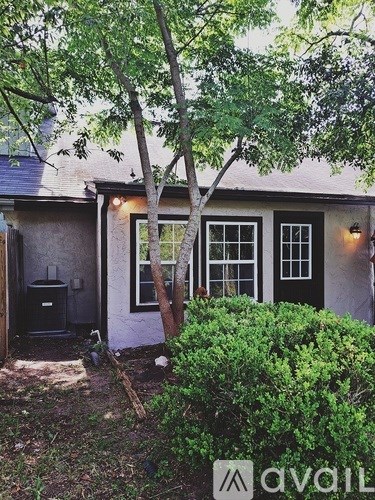 A tree stands in front of a house with a window and a door.