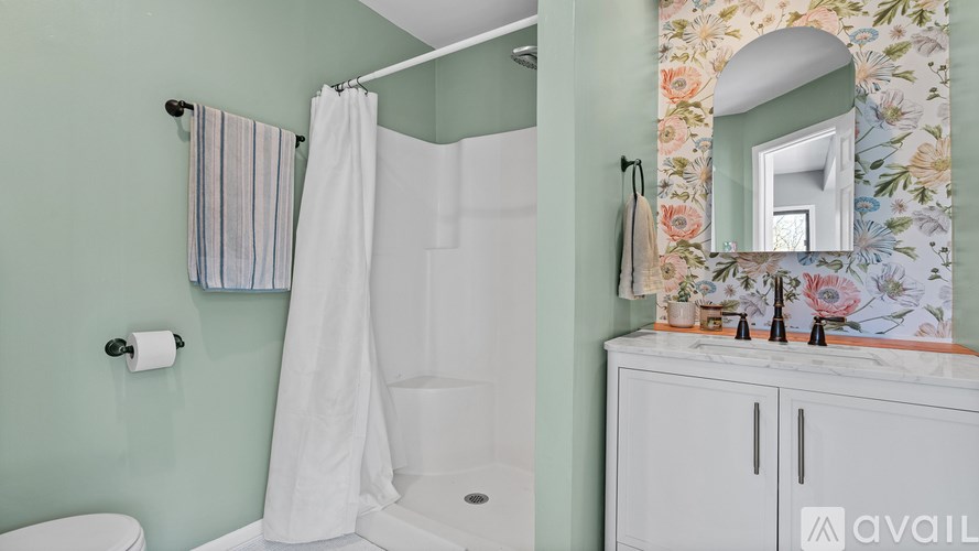 A bathroom with a toilet, a shower with a white curtain, a sink with a mirror and a cabinet.
