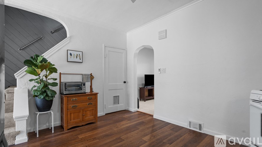 A room with a wooden floor and a white wall with a doorway leading to another room.