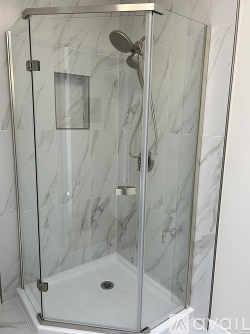 A shower with a glass door and a marble wall.