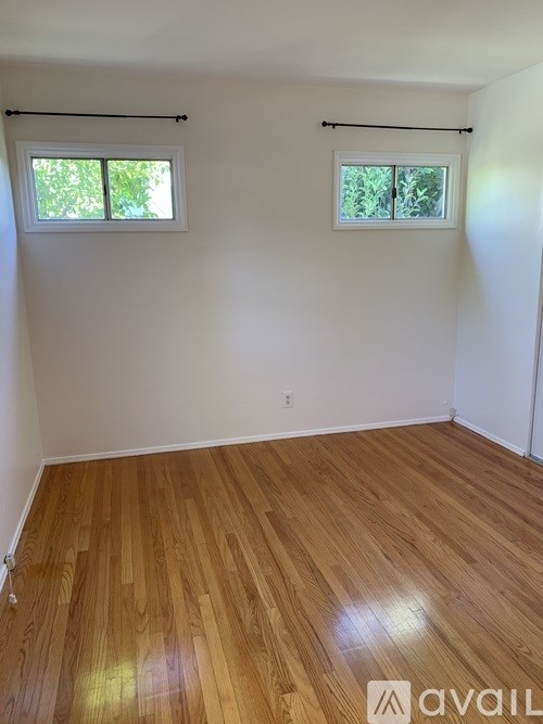 A room with wooden flooring and two windows.