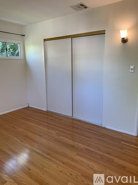 A room with wooden flooring and two windows.
