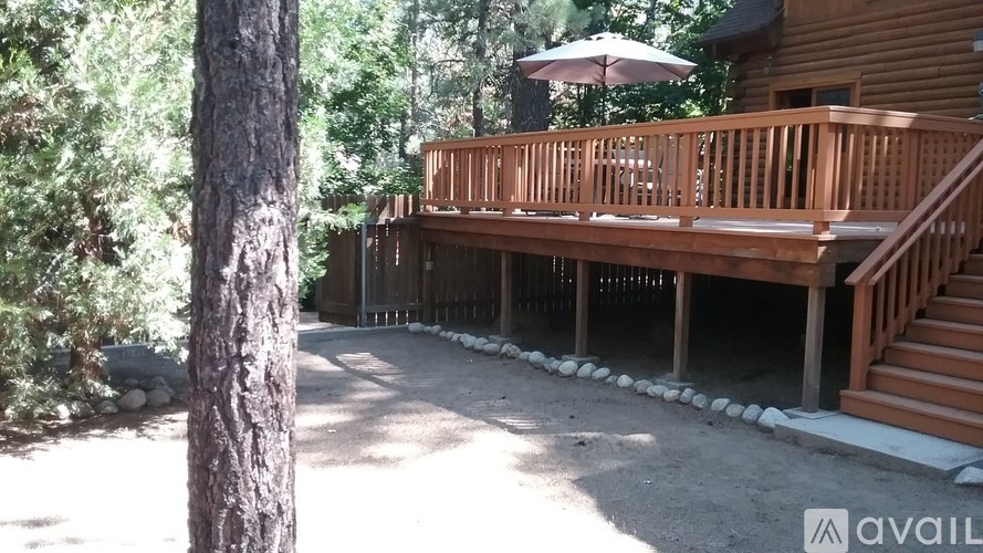 A wooden deck with a staircase leading to a house in a wooded area.