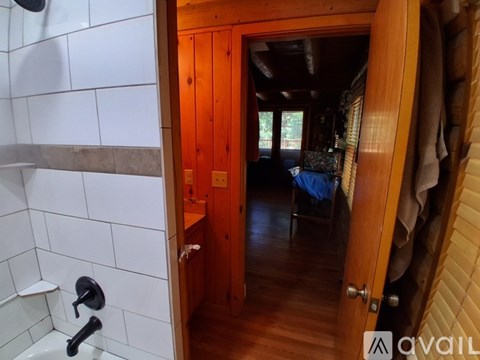 A bathroom with a white tiled shower area and a wooden door leading to a living area.