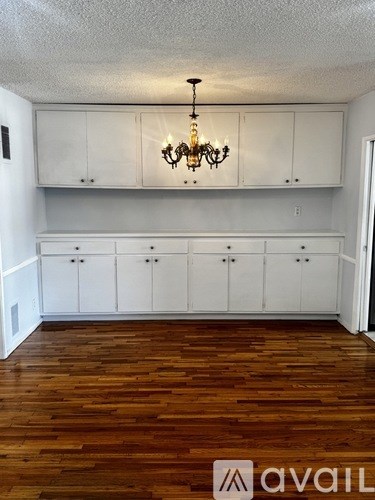 A room with wooden floors and white cabinets with a chandelier hanging from the ceiling.