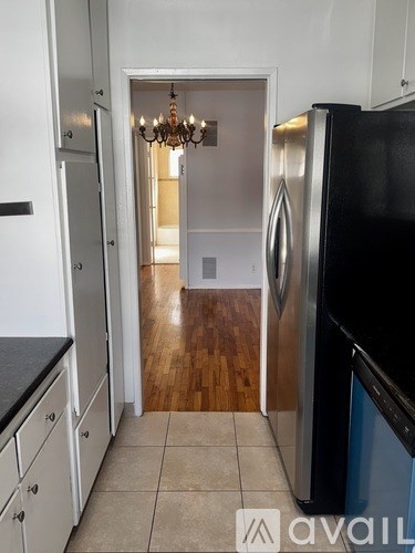A kitchen with a black fridge and a chandelier in the hallway.