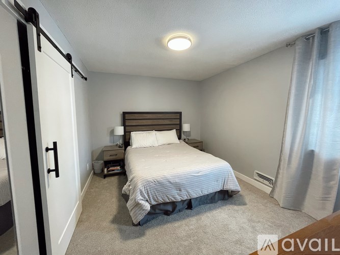 A bedroom with a bed, nightstand, and window with curtains.