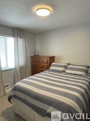A bedroom with a bed, dresser, and window with curtains.