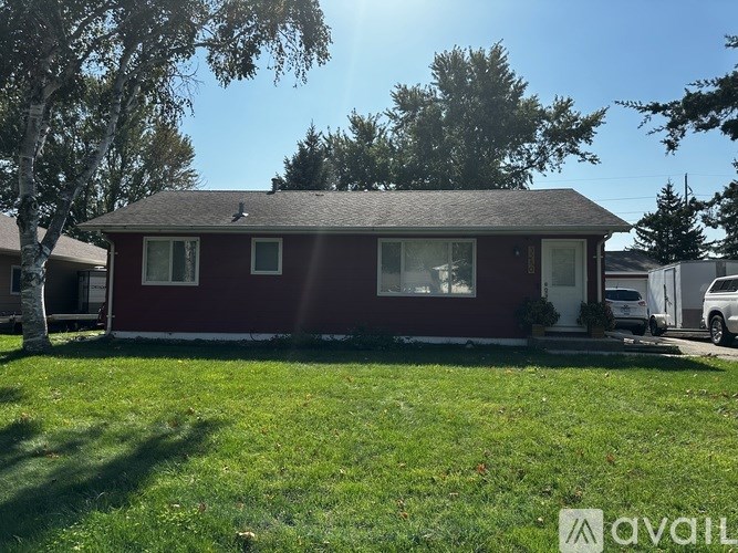 A red house with a white door and windows is surrounded by green grass and trees.