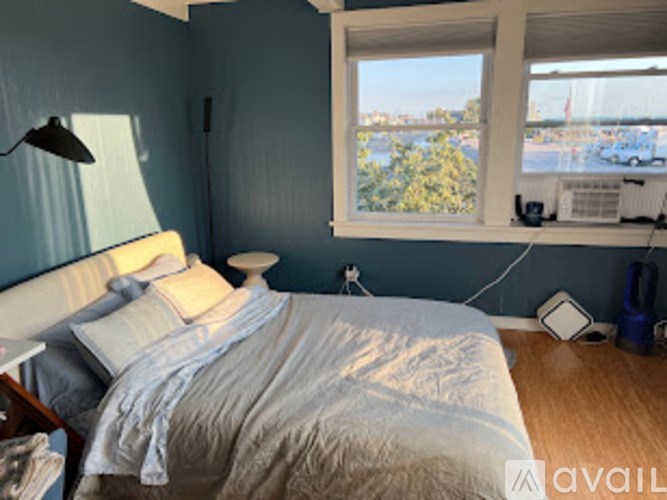 A bedroom with a bed, nightstand, and window overlooking a parking lot.