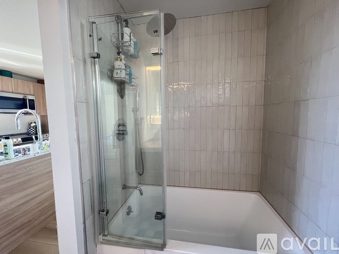 A glass shower stall with a glass door is in a bathroom with white tiled walls.