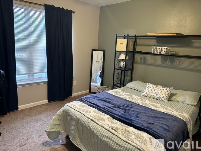 A bedroom with a bed, a window with black curtains, and a shelf with a mirror and some items on it.
