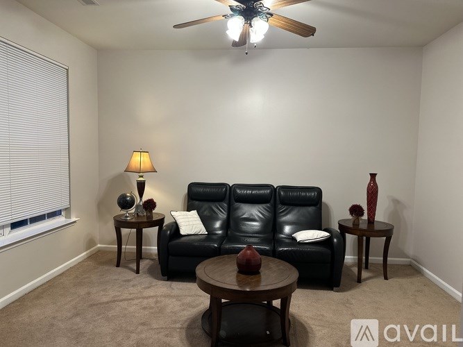 A living room with a black leather couch, a wooden coffee table, and a ceiling fan.