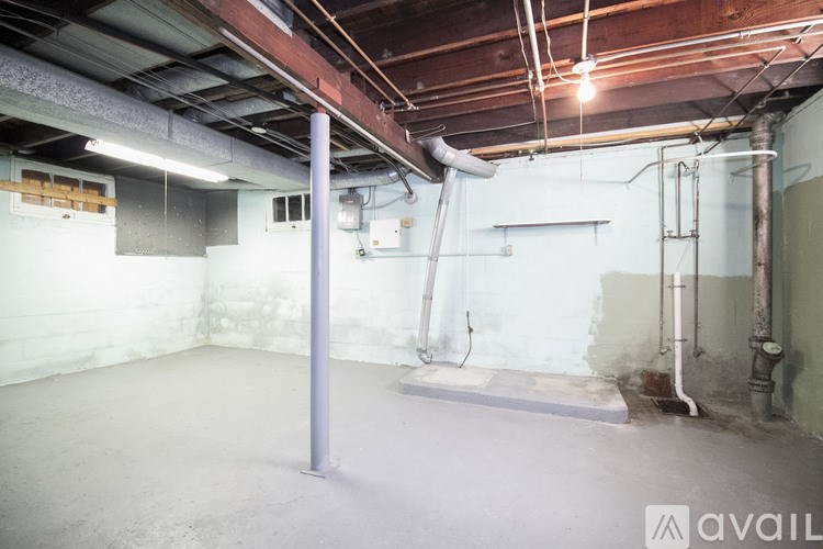A large empty room with a concrete floor and a ceiling covered in duct tape and pipes.