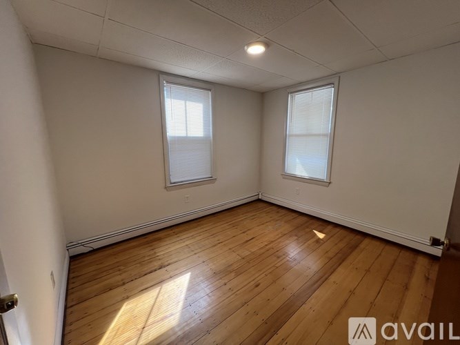 A room with wooden flooring and two windows.