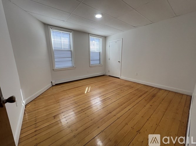 A room with wooden flooring and two windows.